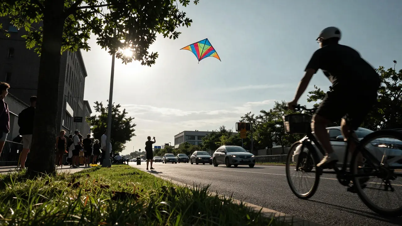 Low angle view of a kite flying over a grassy area near a city street with traffic