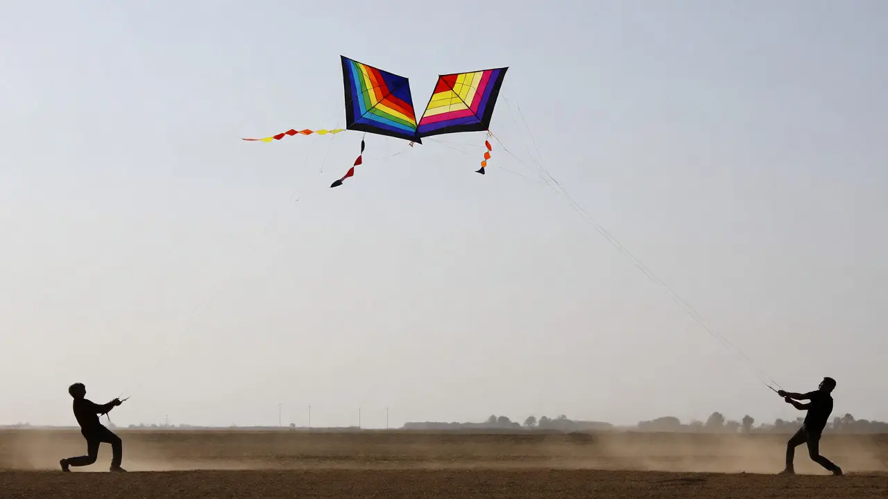 Two kite flyers maneuvering kites closely during a practice session.