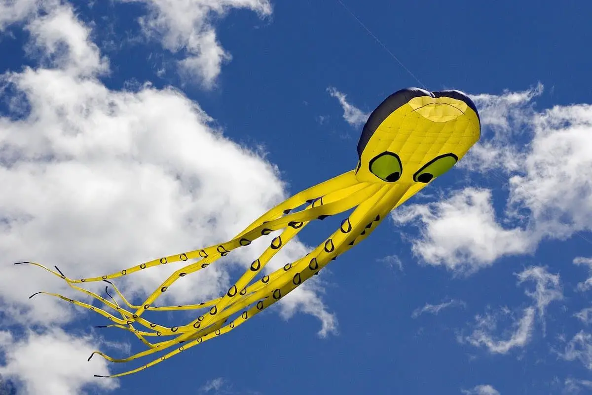 Photo of yellow octopus kite flying against a blue sky with white clouds