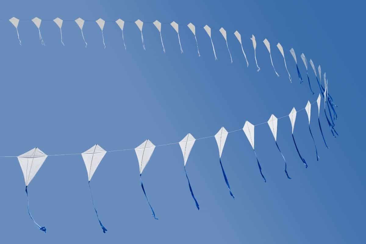 White plastic kites with blue tails against a blue sky