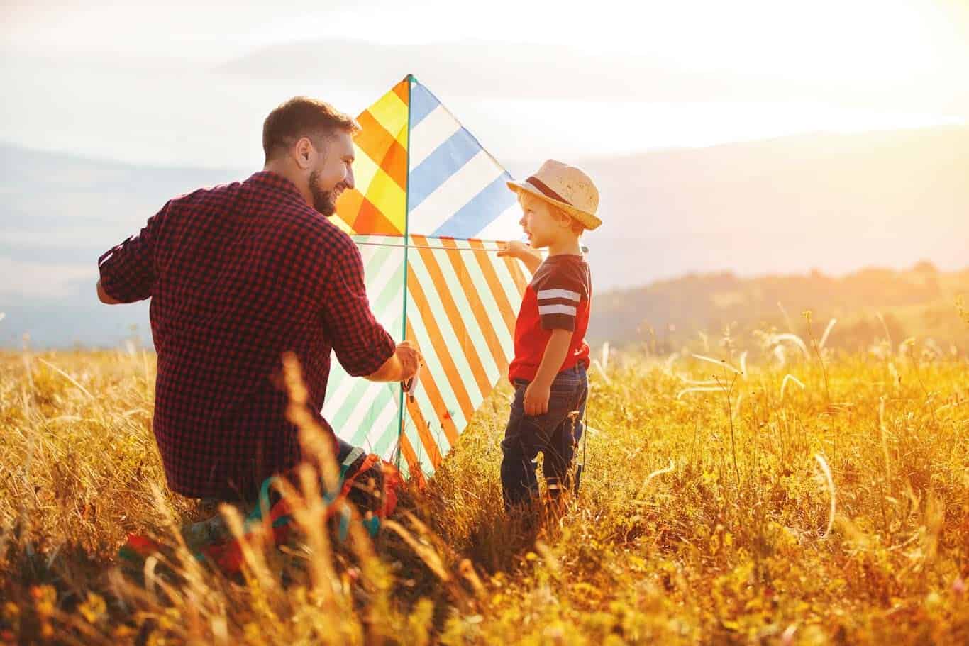 Father and son in field holding a striped kite at sunset