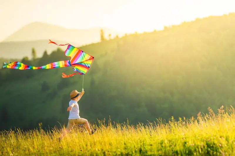 Running through a meadow flying a colorful kite at dawn