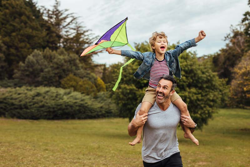 Son on dad’s shoulders flying a kite